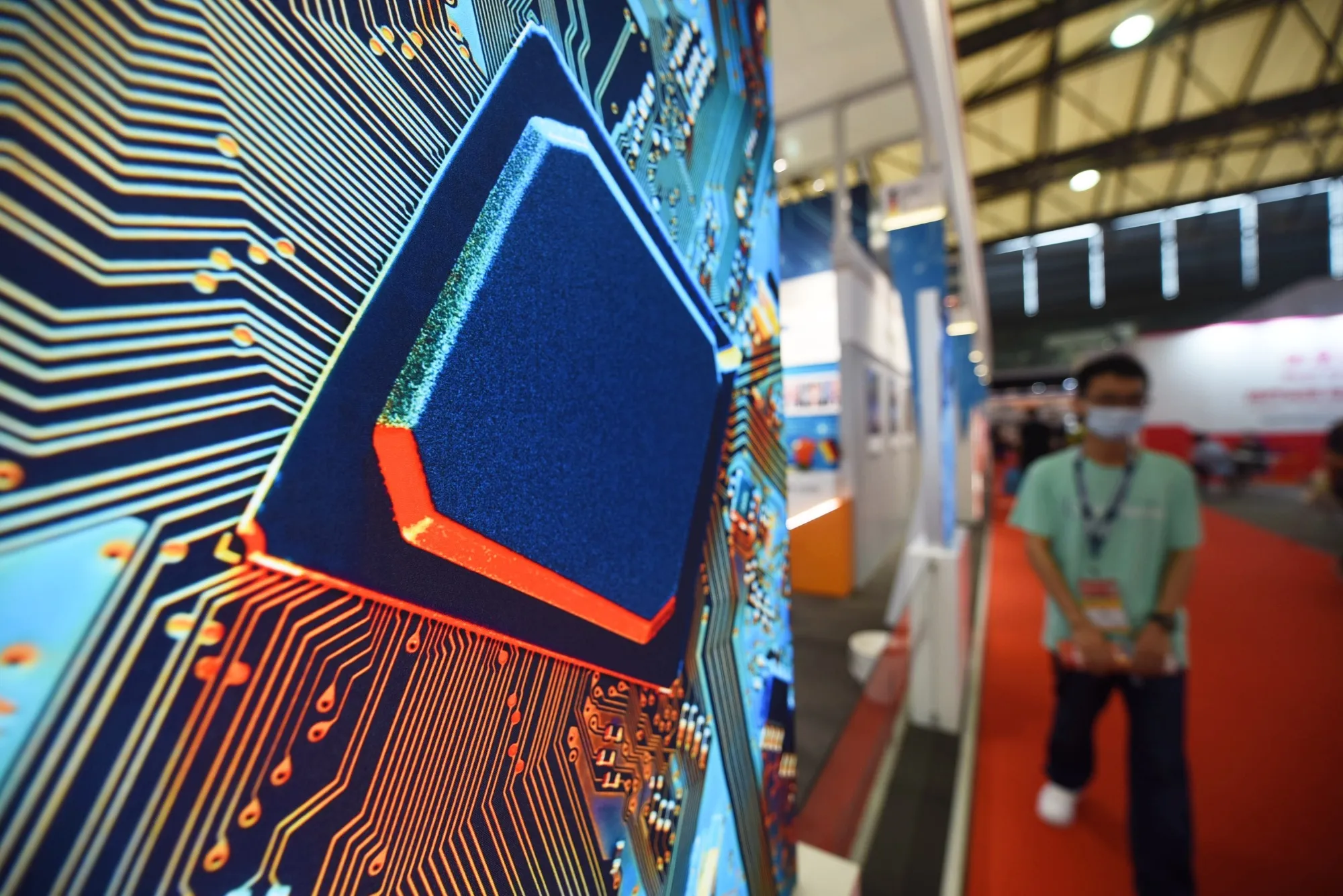 A masked man walks by an image of a circuit board at Semicon China in Shanghai on June 27.