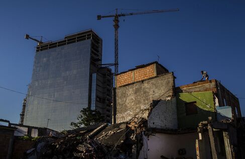 A woman checks a water reservoir on the rooftop of a partially destroyed home near construction of hotel towers for the 2016 Olympic Park in the Vila Autodromo favela of Rio, on June 10, 2015.