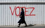 A woman walks past graffiti on a fence that reads, 'Vote', in Paris, France.
