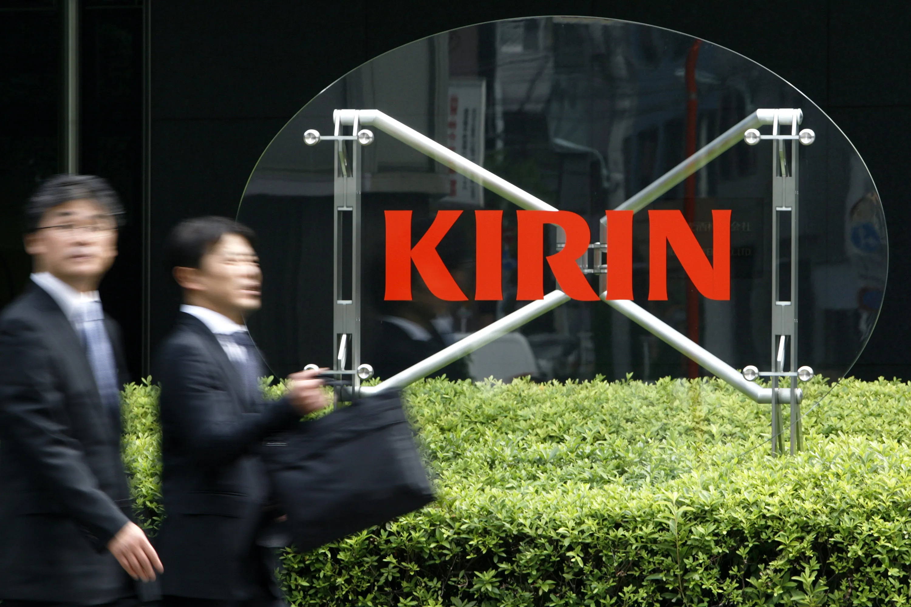 People walk past a sign at the Kirin Holdings Co. headquarters in Tokyo.