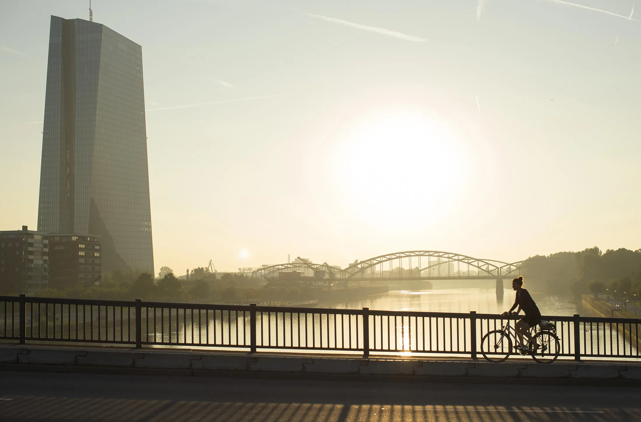 A cyclist rides across a bridge as the skyscraper headquarters of the European Central Bank (ECB) stands beside the River Main in Frankfurt, Germany, on Thursday, Sept. 8, 2016.
