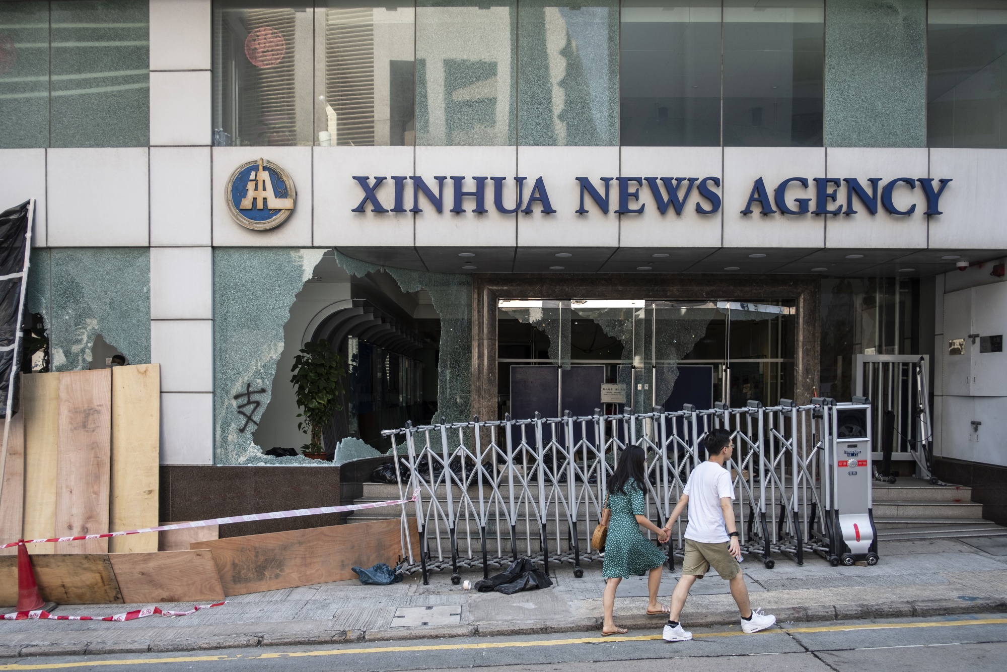 Pedestrians walk past a vandalized entrance to the offices of Xinhua News Agency following a protest in Hong Kong, China, on&nbsp;Nov. 3, 2019.&nbsp;
