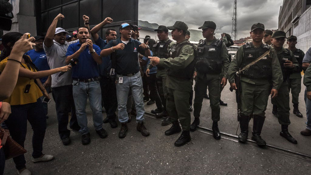 Workers at a food distribution center, left, react to Venezuelan soldiers who took over the warehouse where they were working in Caracas, Venezuela, on July 30, 2015.
