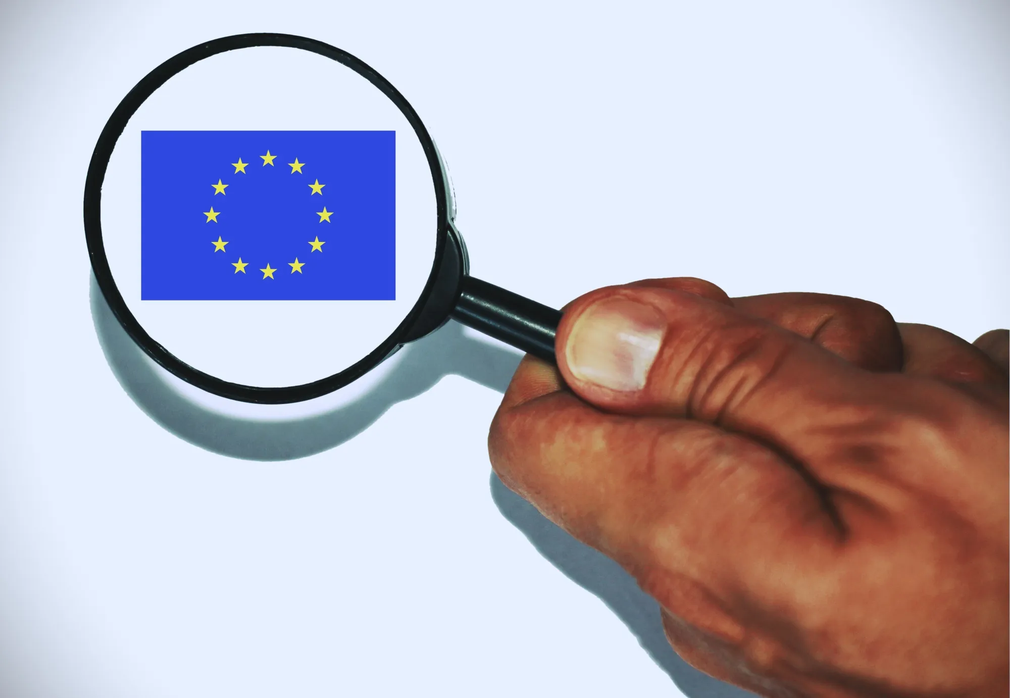 Hand holding a Magnifier glass showing the European Flag .