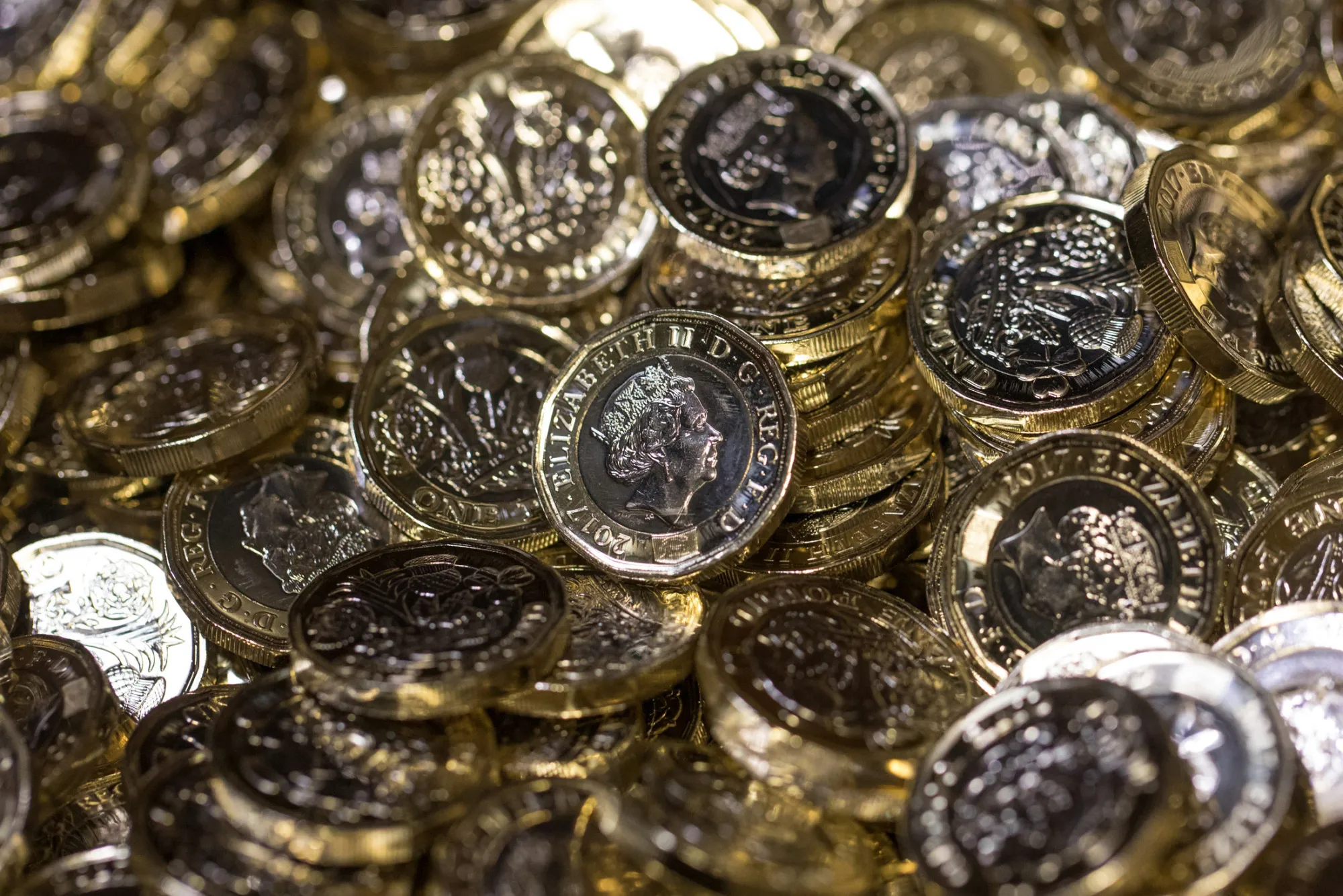 New British one pound coins sit in a container during their production at The Royal Mint in Llantrisant, U.K., on Thursday, March 23, 2017. Britain's Royal Mint is making 1.5 billion new one pound coins, which will enter circulation on Tuesday, with security features such as a unique 12-sided, bimetallic design, a hologram, fine lettering and some secret tricks to beat crooks.
