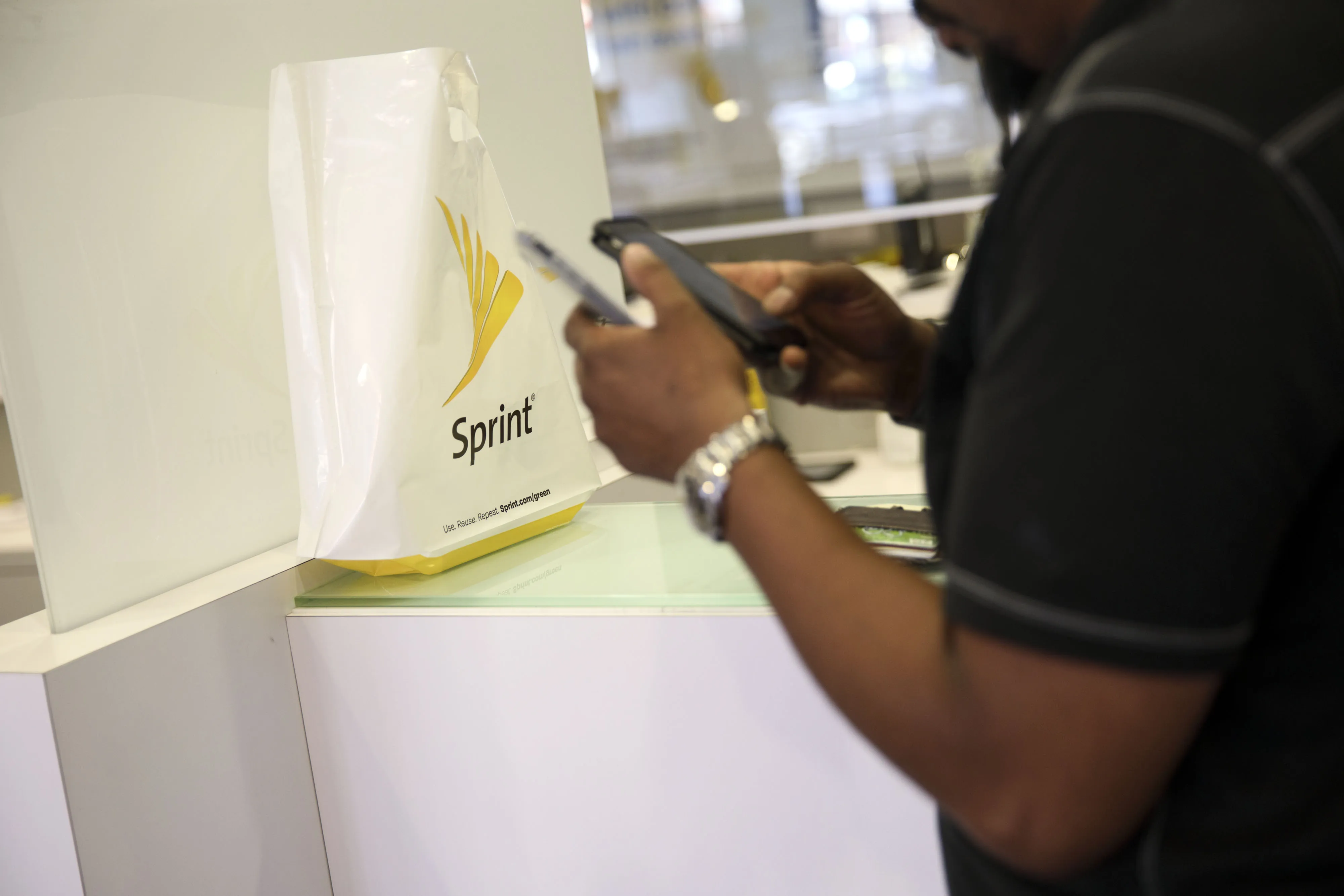 A shopping bag sits on a counter as a customer uses a mobile device at a Sprint Corp. store in Glendale, California, U.S., on Monday, April 24, 2017.&nbsp;