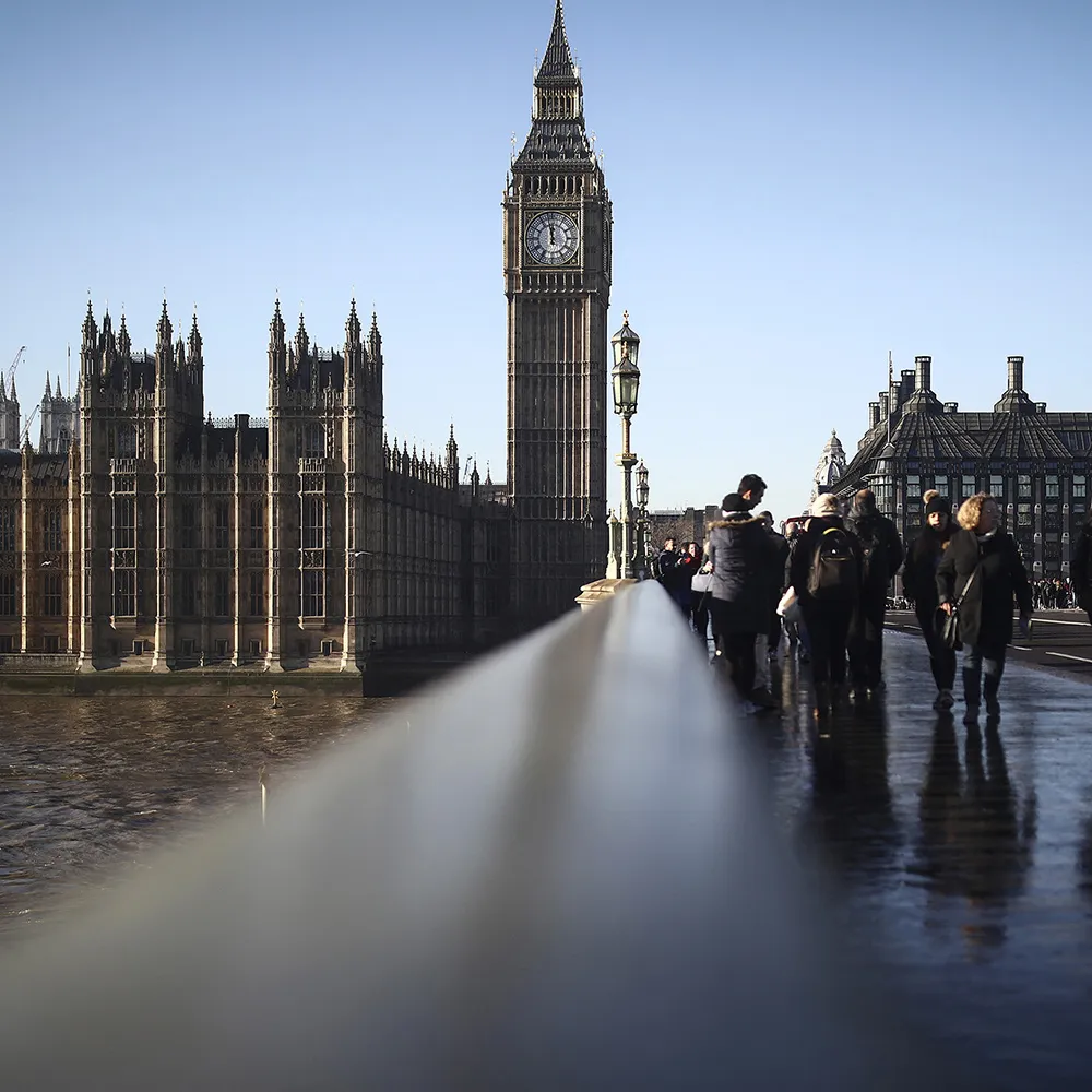 Tourists cross Westminster Bridge beside the Houses of Parliament in London.
