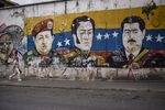 A pedestrian passes in front of a mural depicting the late Hugo Chavez, Simon Bolivar, and Nicolas Maduro, Venezuela's president, in the Palo Verde neighborhood of Caracas.