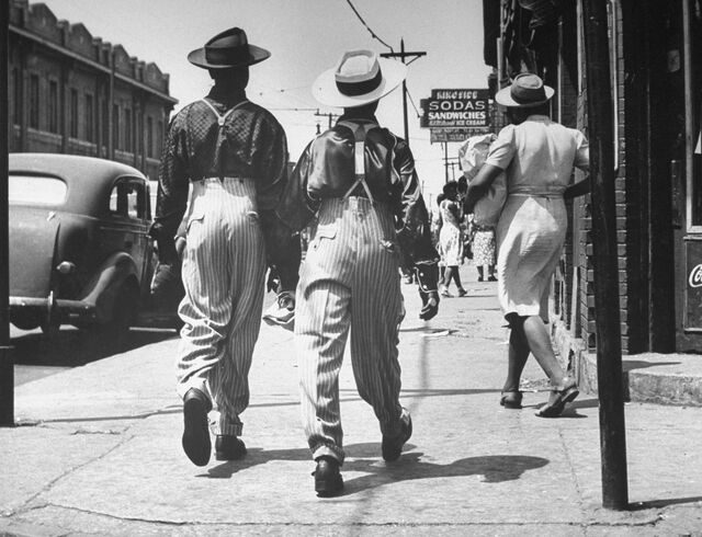 Ζευγάρι μαύρων ανδρών που φορούν κοστούμι ζωού, περπατούν στο δρόμο μετά από ταραχές αγώνων εν καιρώ πολέμου.
