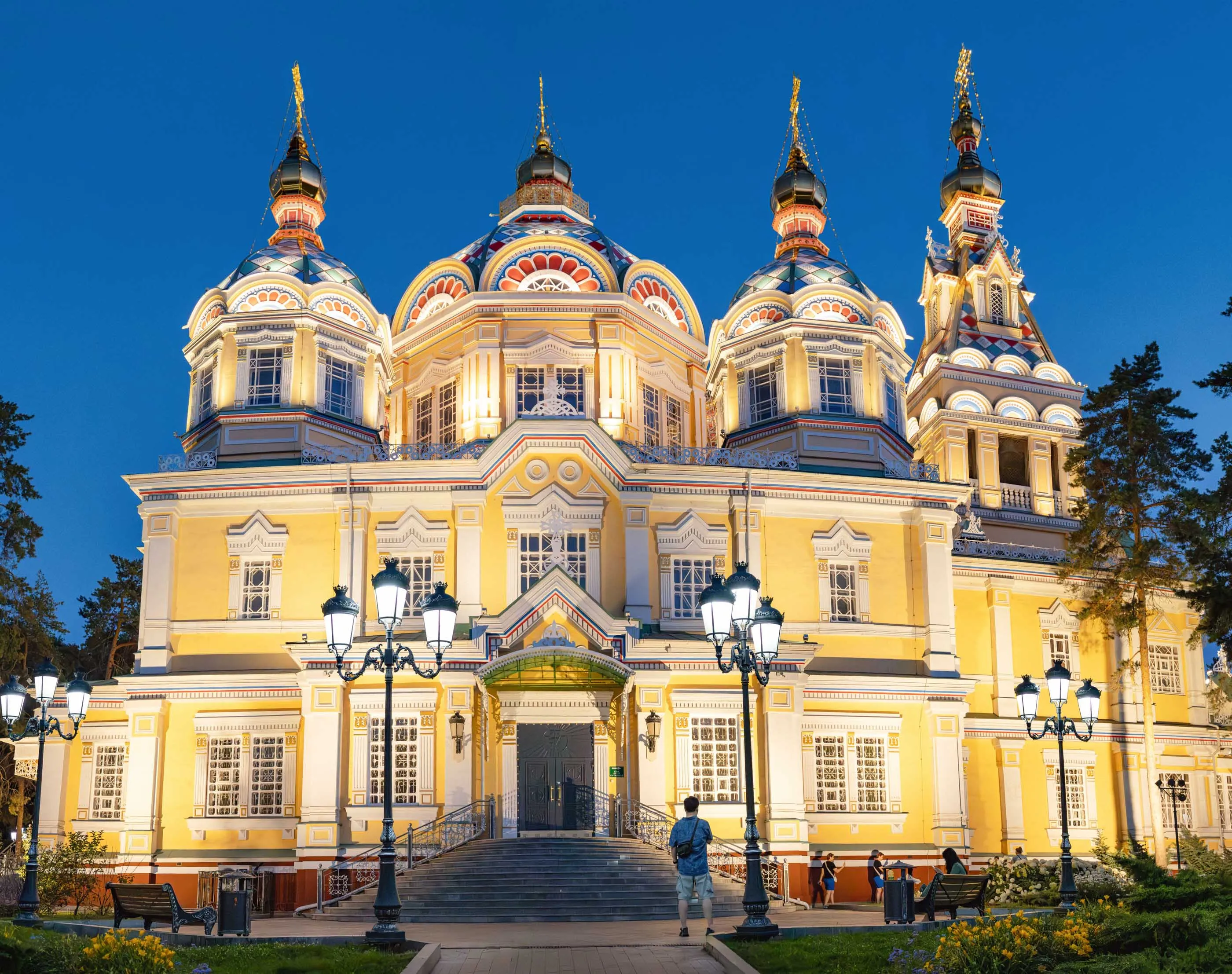 A Russian Orthodox church with a bright yellow facade against the twilight Almaty sky.