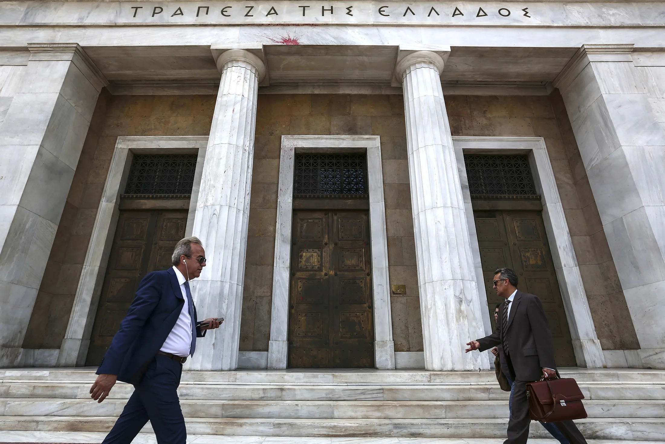 Pedestrians pass the entrance to the headquarters of the Bank of Greece in Athens, Greece, on Thursday, May 26, 2016. Greece may have passed a milestone and its bond market has been lucrative for some investors, but the road to recovery doesn't look much shorter.

