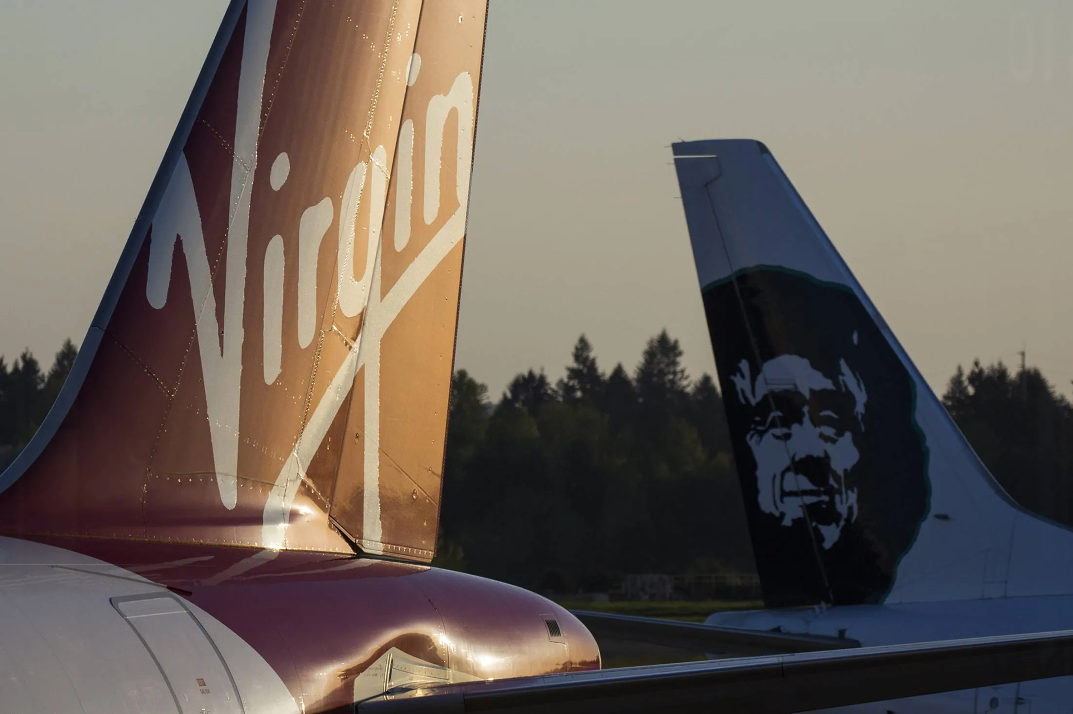 The tails of a Virgin America Inc. plane, left, and an Alaska Air Group Inc. jet are seen at Seattle-Tacoma International (SEA) airport in Seattle, Washington, U.S., on Saturday, April 9, 2016. Alaska Air agreed to buy Virgin America for $2.6 billion, overcoming interest in the Richard Branson-backed carrier from JetBlue Airways Corp. to secure a deal that bolsters its main West Coast business while opening up key airports in New York and Washington.
