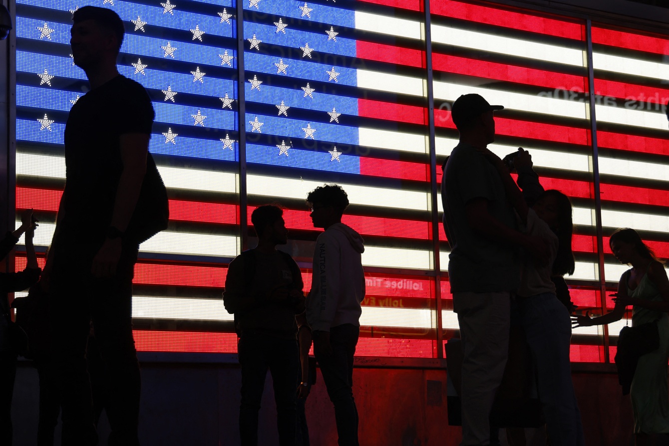 People stand in front of a US flag on a screen in Times Square in New York. Photographer: Ludovic Marin/AFP/Getty Images