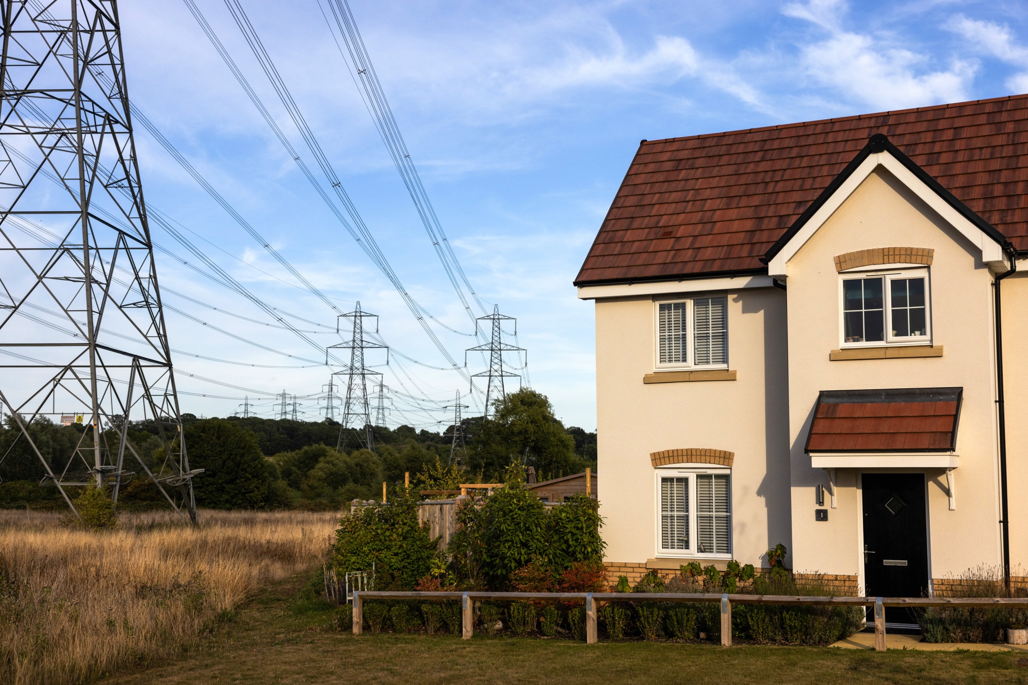 Electricity pylons next to a new house on a residential housing development in Bramford, UK, on Tuesday, Aug. 26, 2025. The energy price cap — set every three months by Ofgem — will rise to £1,755 ($2,361) from Oct. 1, the regulator said Wednesday in a statement.