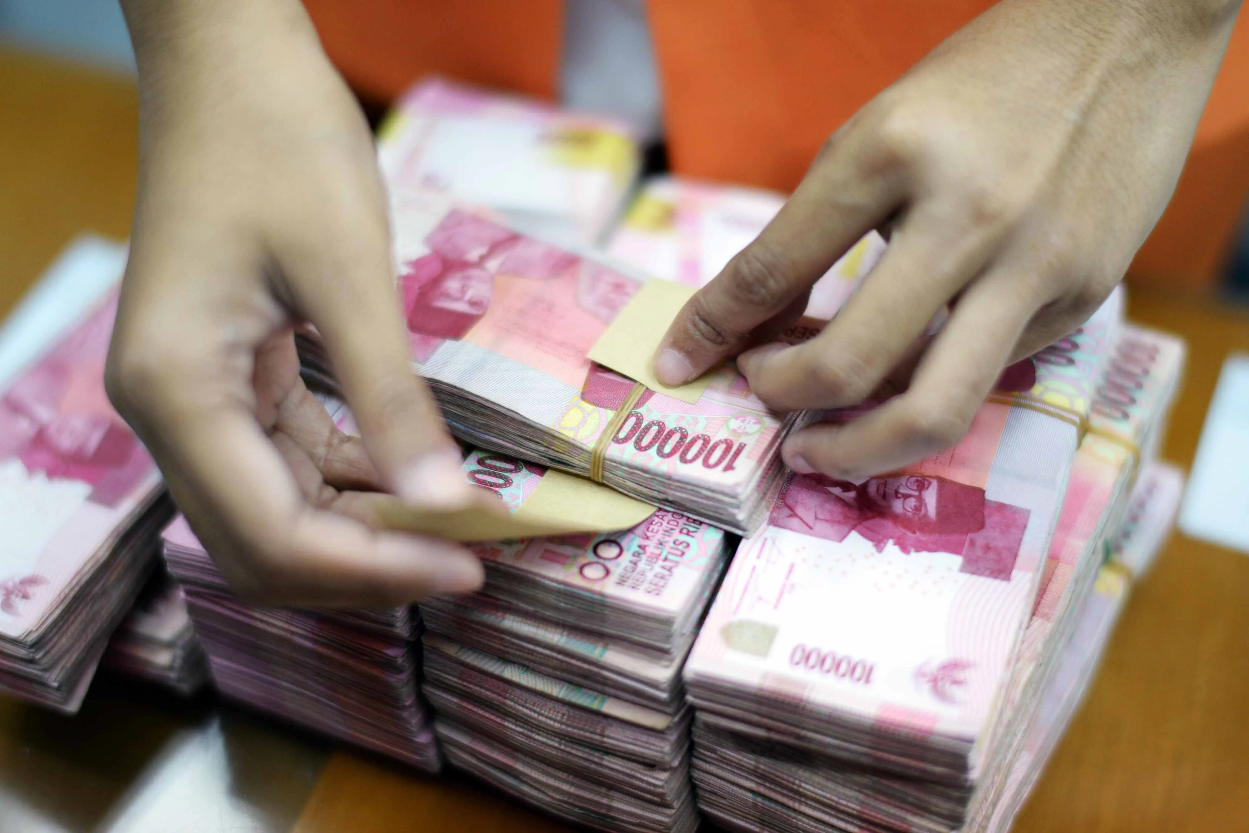 A clerk arranges bundles of Indonesian 100,000 rupiah banknotes at a currency exchange office.
