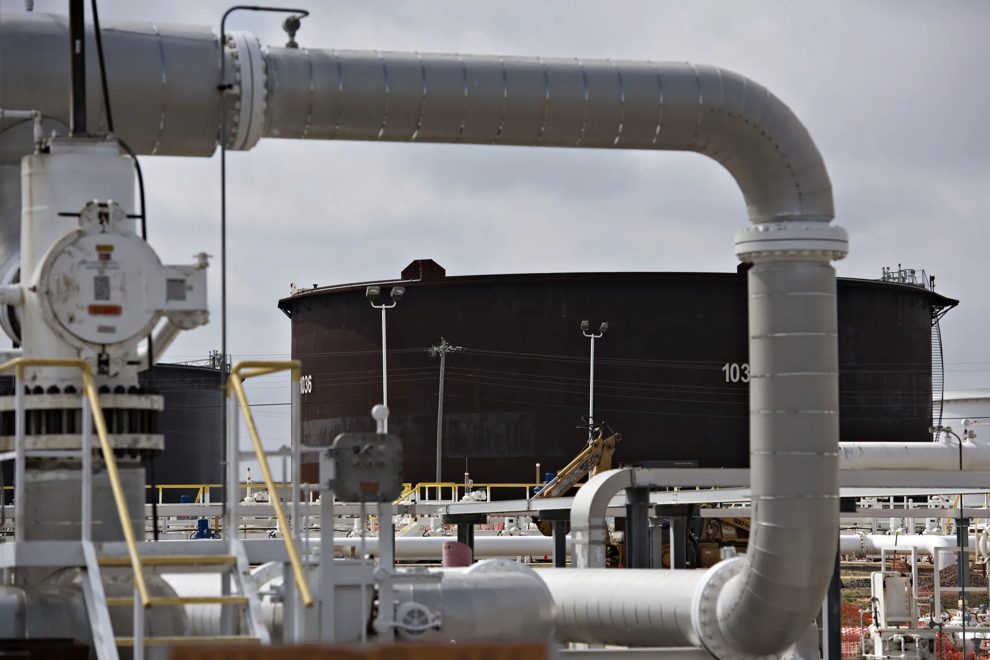 A crude oil storage tank stands beyond a manifold at an Enbridge storage terminal in Cushing, Oklahoma.