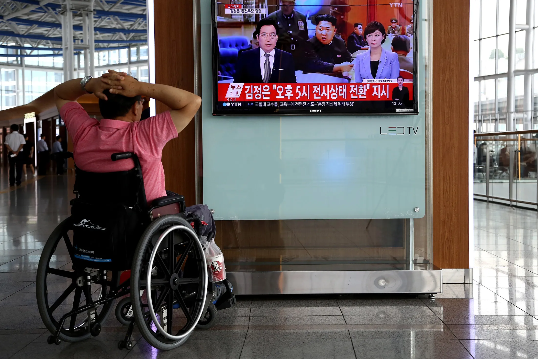A man sitting on a wheelchair looks at a television screen showing an image of Kim Jong Un, leader of North Korea, center, during a news broadcast on North Korea's exchange of fire with South Korea at Seoul Station in South Korea.
