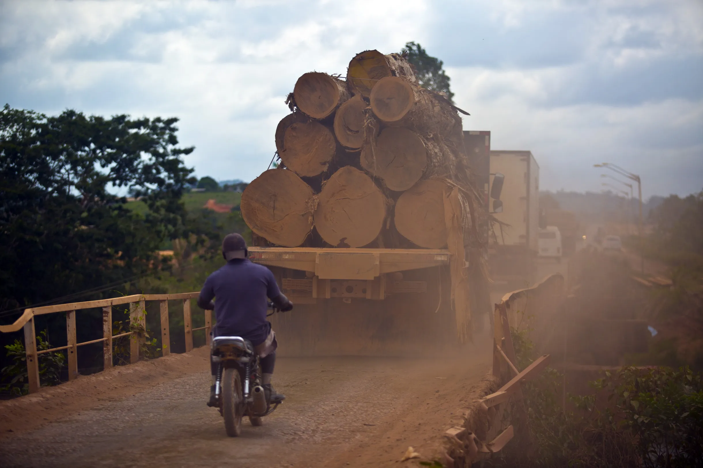 A man rides a motorcycle behind a truck hauling cut logs to a sawmill in Anapu, Brazil.