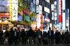 Pedestrians cross a street illuminated with neon signs in Tokyo.