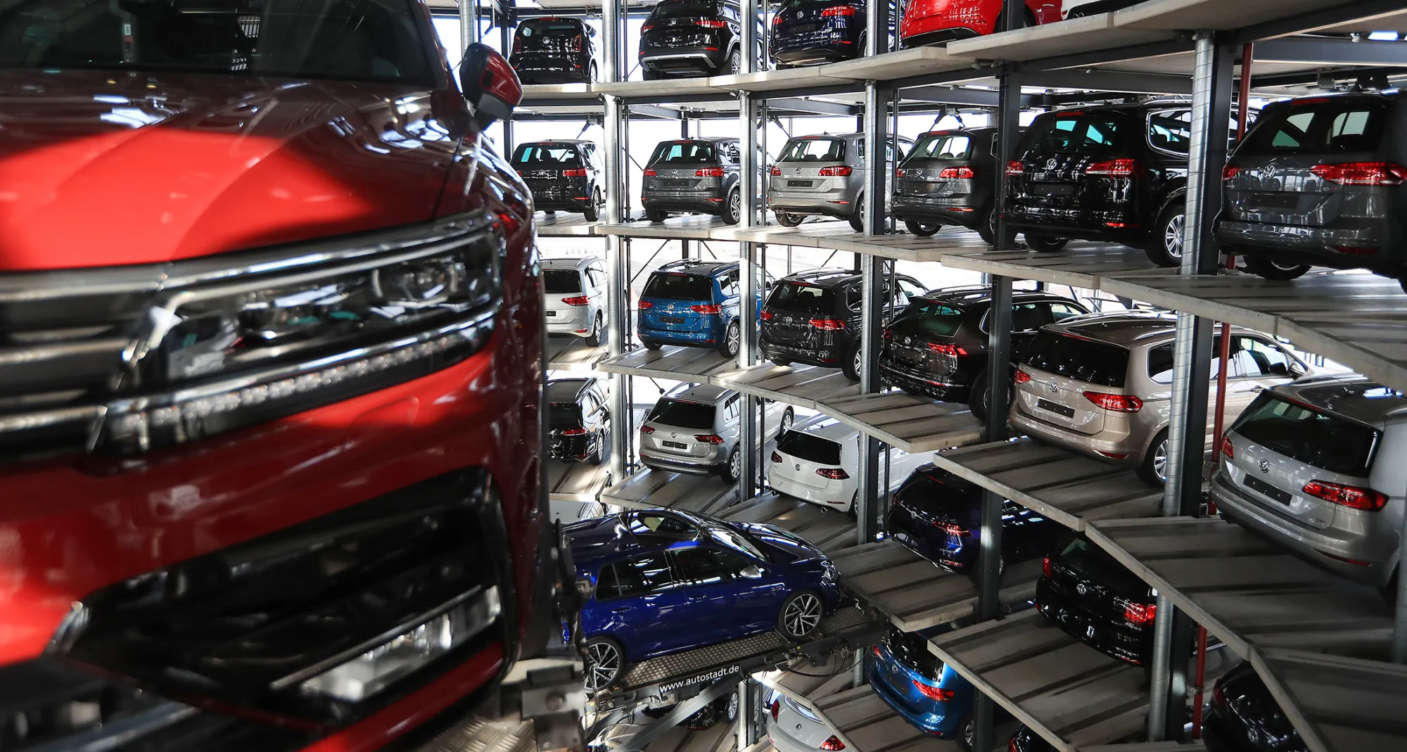 A new Tiguan sports utility vehicle (SUV), produced by Volkswagen AG (VW), left, is transported on an elevation platform as new VW automobiles sit in storage bays inside one of the automaker's glass delivery towers at the VW factory in Wolfsburg, Germany, on Tuesday, March 14, 2017. Volkswagen sought to draw a line under the diesel scandal that has locked it in crisis mode for more than a year, with sweeping restructuring efforts starting to take hold and profitability improving at the namesake auto brand.
