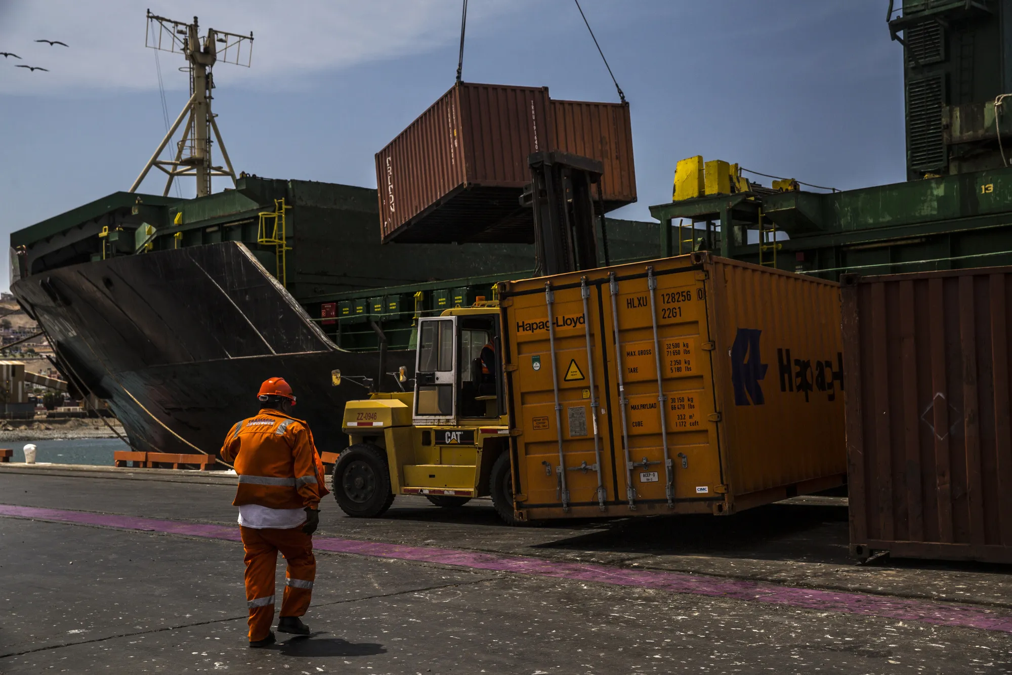 A longshoreman passes in front of shipping containers filled with copper plates being loaded onto a ship at the Port Terminal of Ilo, Peru.
