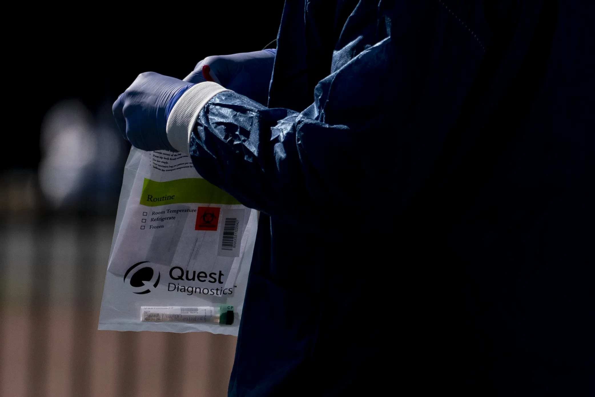 A&nbsp;healthcare worker holds a Quest Diagnostics bag containing a Covid-19 swab.