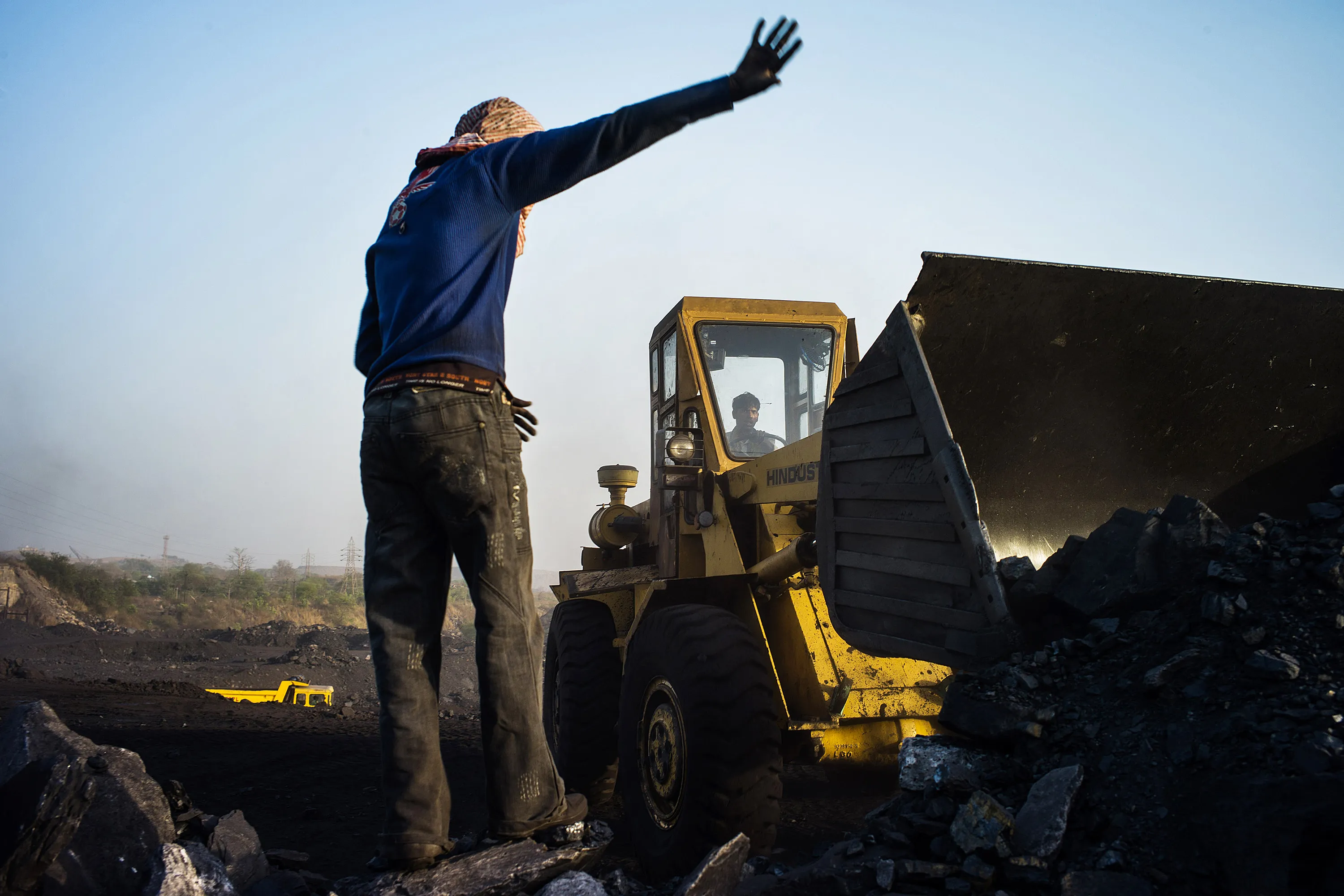 A worker directs a loader collecting coal at the Goladi coal depot, in Jharia, Jharkhand, India.
