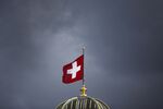 The Swiss national flag flies above the Federal Palace, Switzerland's parliament building in Bern, Switzerland, on Tuesday, March 12, 2013. The Swiss central bank pledged to keep up its defense of the franc cap after almost doubling its currency holdings to shield the country from the fallout caused by the euro zone's crisis.
