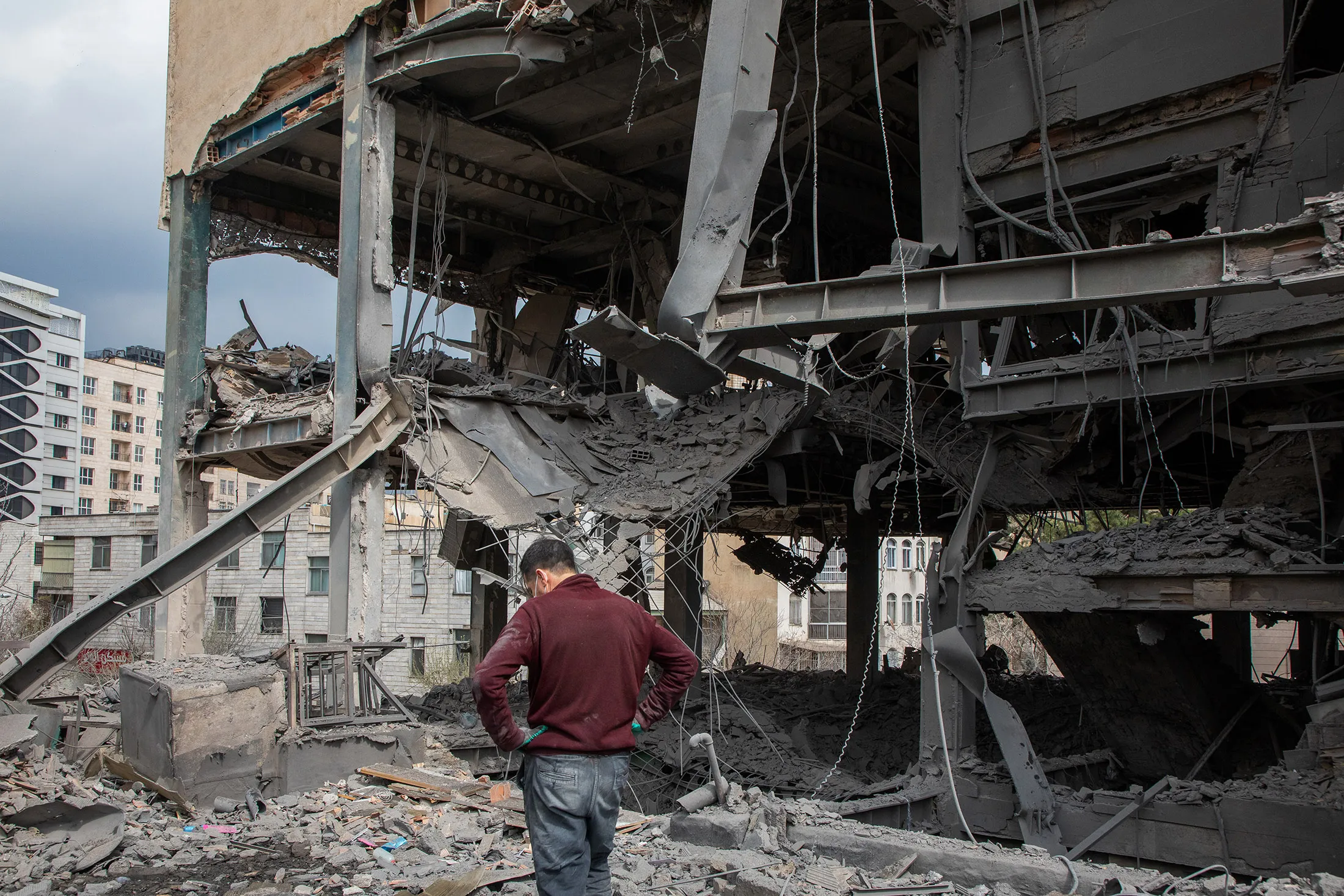 A person surveys damage at the site of a building hit by a strike on a commercial district in Tehran.