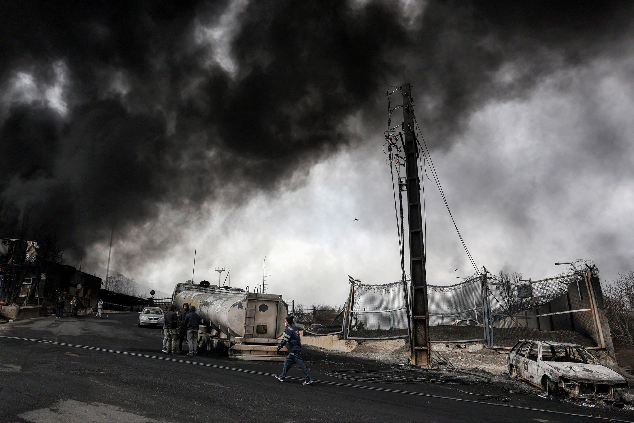 Dark smoke clouds engulf destroyed vehicles near an ongoing fire following an overnight airstrike on the Shahran oil refinery in northwestern Tehran on March 8.