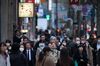 Pedestrians wearing face masks wait to cross a road in the Shinbashi district in Tokyo, Japan.