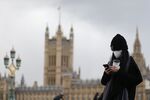 A pedestrian wearing a face mask walks along Westminster Bridge in front of the Houses of Parliament in London on March 12, 2020.