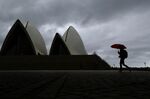 A pedestrian holding an umbrella walks past the closed Sydney Opera House stands in Sydney, Australia, on Tuesday, March 24, 2020. Australia's parliament rushed through more than A$80 billion ($46.3 billion) in fiscal stimulus for the coronavirus-stricken economy at a special sitting in Canberra on March 23.