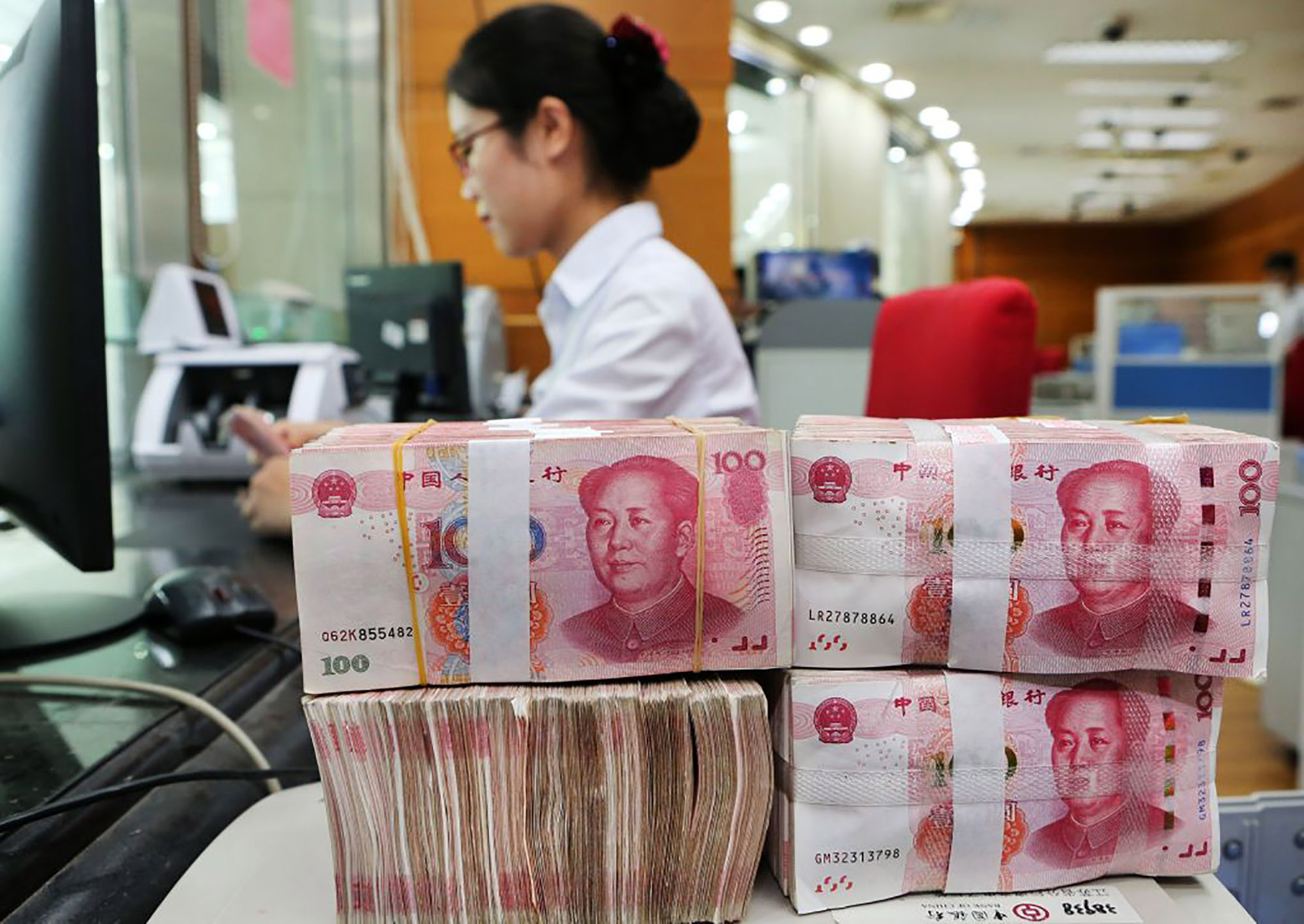 An employee counts 100-yuan notes at a bank in Nantong, Jiangsu province, China.&nbsp;