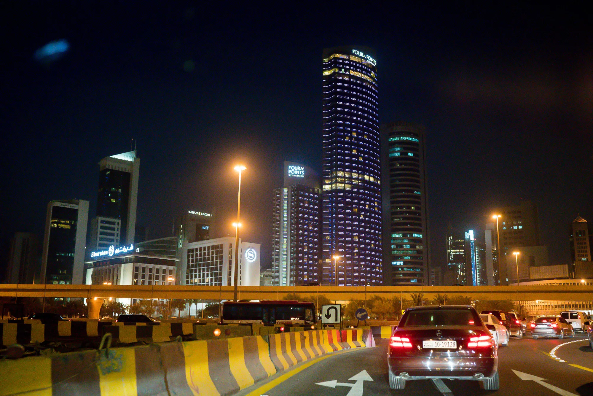 Automobiles drive along a highway past skyscrapers in Kuwait City.
