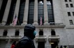 A woman with a facial mask passes the New York Stock Exchange. 