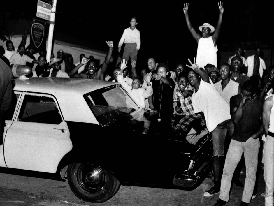Demonstrators push against a police car in the Los Angeles area of Watts on August 12, 1965. 