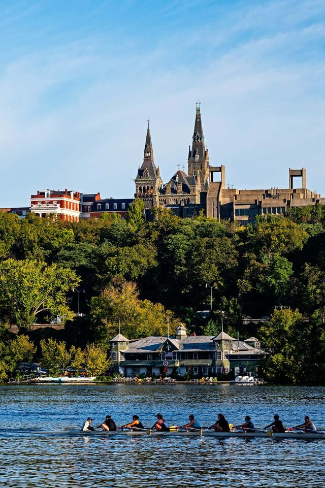 A crew team passes by the Washington Canoe Club and the Georgetown University campus on the water.