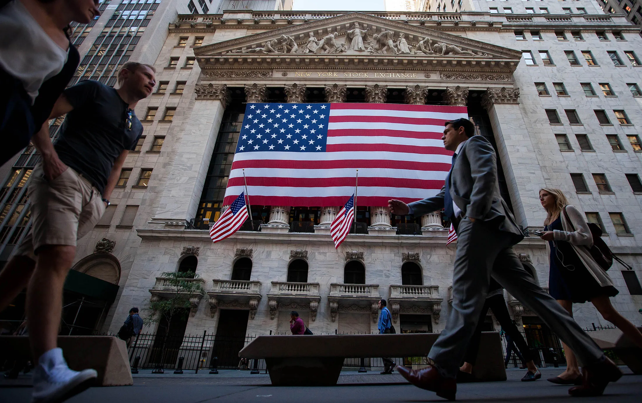 Pedestrians walk past an American flag displayed outside of the New York Stock Exchange (NYSE) in New York, U.S.

