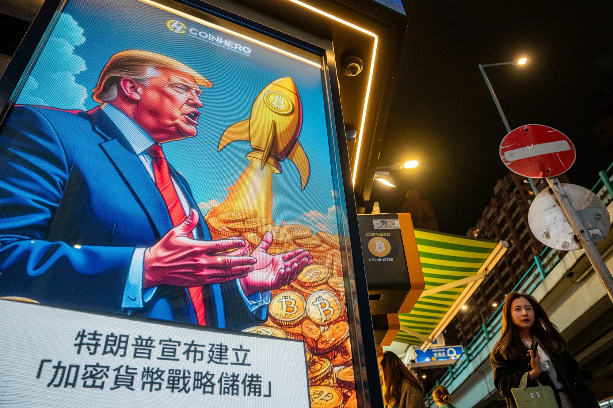 A person walks past a cartoon image of US President Donald Trump with Bitcoin tokens at a Coinhero store in Hong Kong, China, on Friday, March 7, 2025.