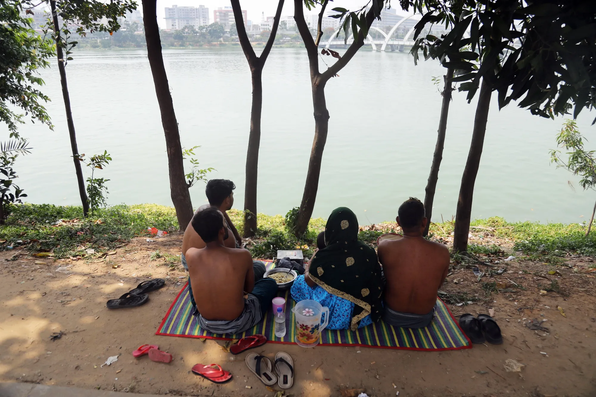 People sit in front of a lake during high temperatures in Dhaka, Bangladesh, on Tuesday, June 6, 2023. Carbon-dioxide emissions from burning fossil fuels are trapping heat in the atmosphere. That's warming the planet and is the primary driver of more extreme weather events, including heat waves.