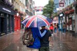 Tourists shelter from the rain under an umbrella featuring an Union flag, also known as a Union Jack, in London, U.K., on Monday, Aug. 13, 2018.