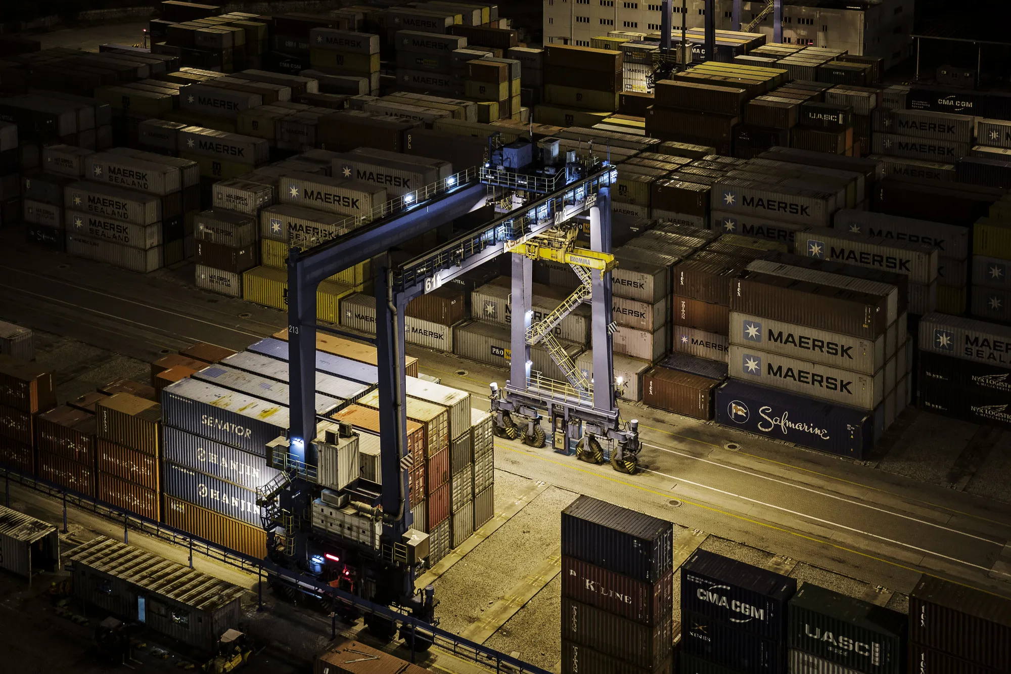 A gantry crane stands next to shipping containers stacked at the Xiamen Songyu Container Terminal at night in Xiamen, China, on Saturday, Jan. 30, 2016.