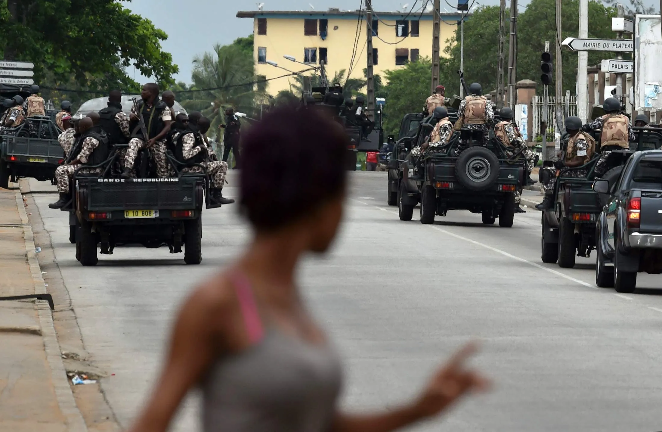 A woman walks past Ivorian soldiers patrolling by Ivory Coast's army headquarters, the Gallieni military camp, in Abidjan on May 12, 2017.
