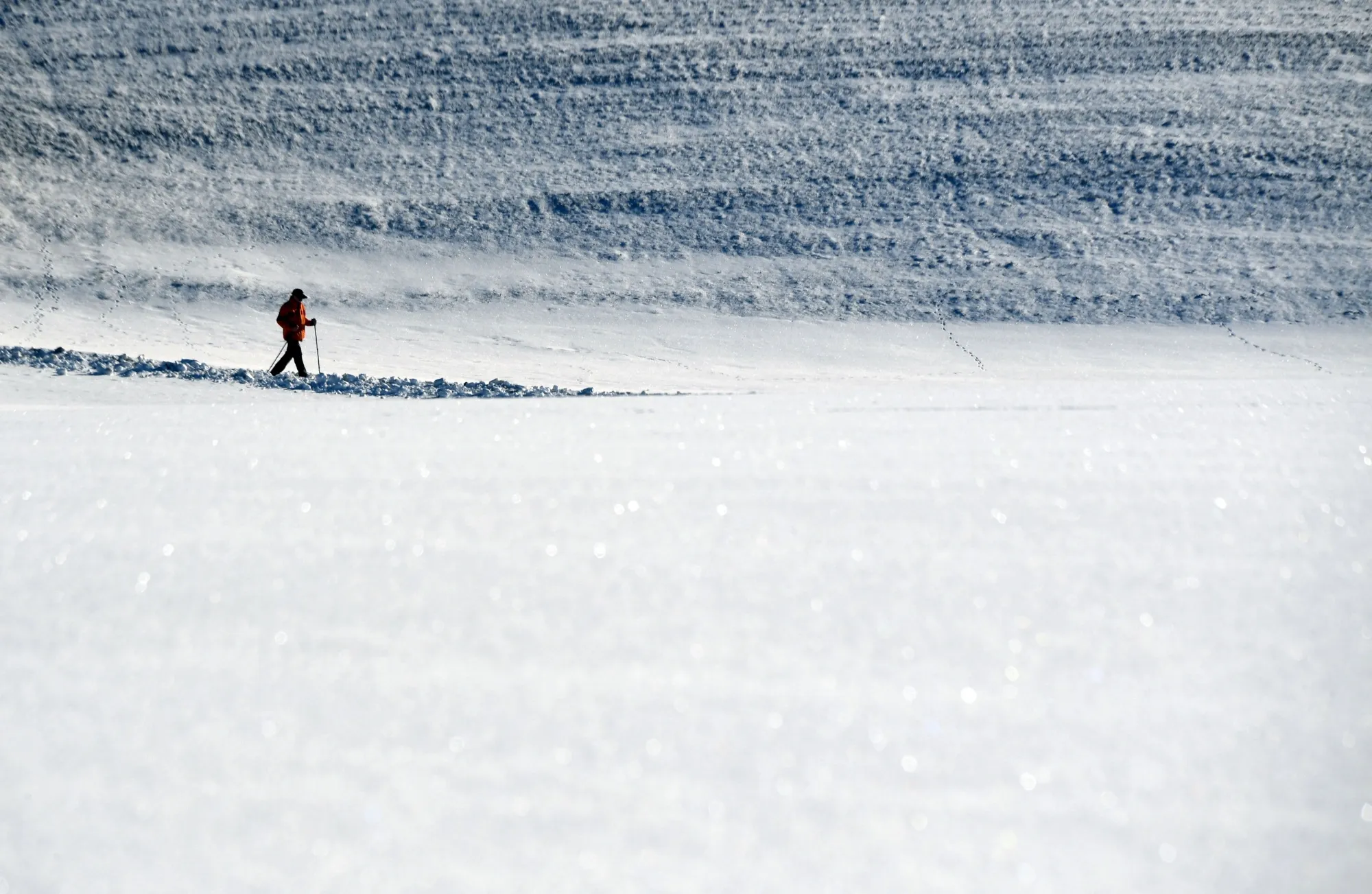 A hiker walks in a snowy landscape in front of the Alps mountains.