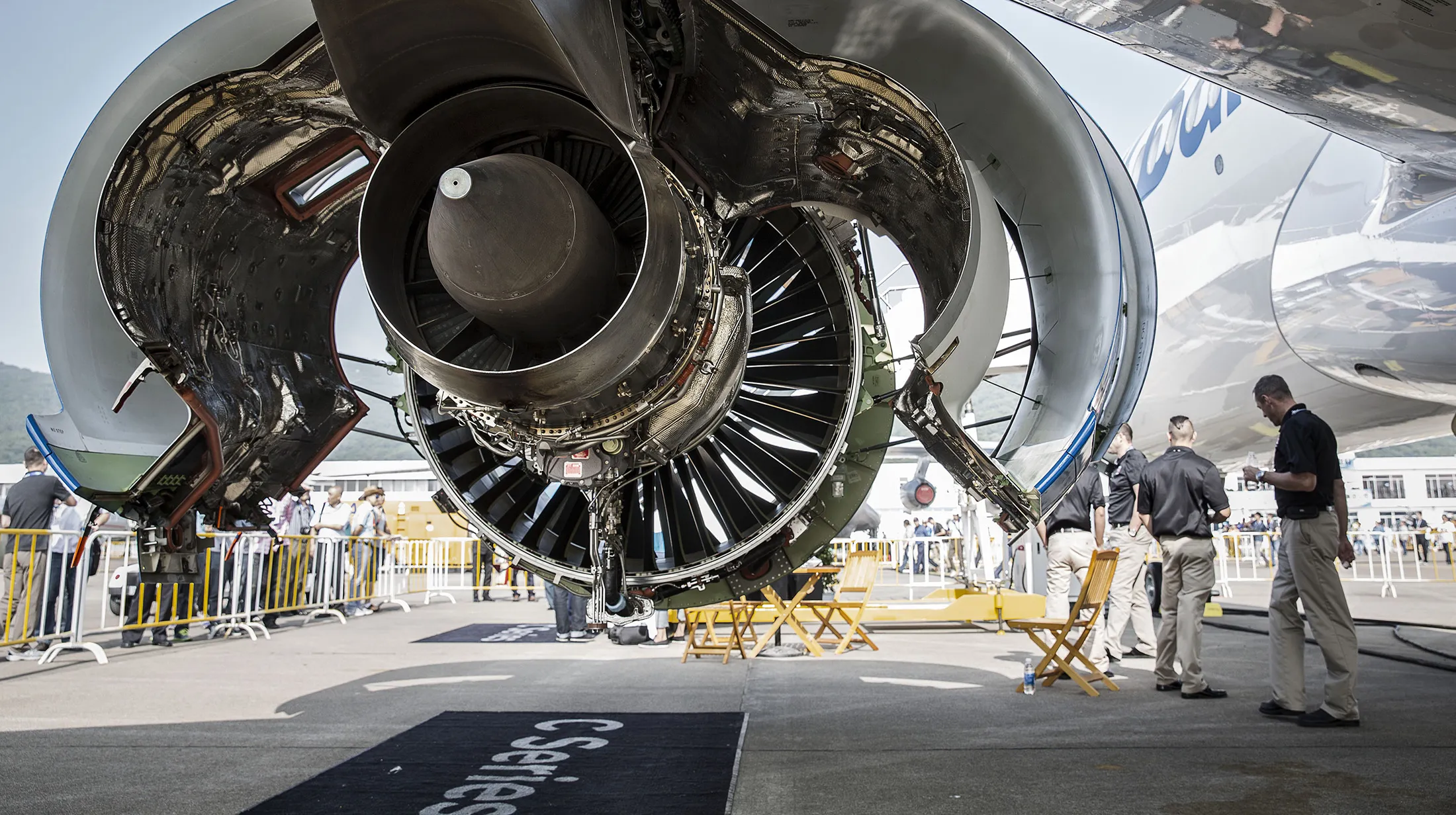 Technicians stand next to an engine on a Bombardier Inc. CS300 passenger jet.

