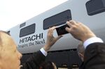 A member of the media uses a smartphone to photograph a Class 800 Intercity Express train, produced by Hitachi Ltd., as it stands on the dockside following its unloading from the Tamerlane roll-on roll-off transporter ship, operated by Wallenius Wilhelmsen, at the Port of Southampton in Southampton, U.K., on Thursday, March 12, 2015. The five-car train produced for the Great Western train route, is one of 12 to be built at Hitachi's Kasado Works, with the remaining 110 to be manufactured at the company's new Newton Aycliffe site in the U.K..