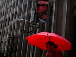 A woman carries a red umbrella while walking along Wall Street near the New York Stock Exchange.