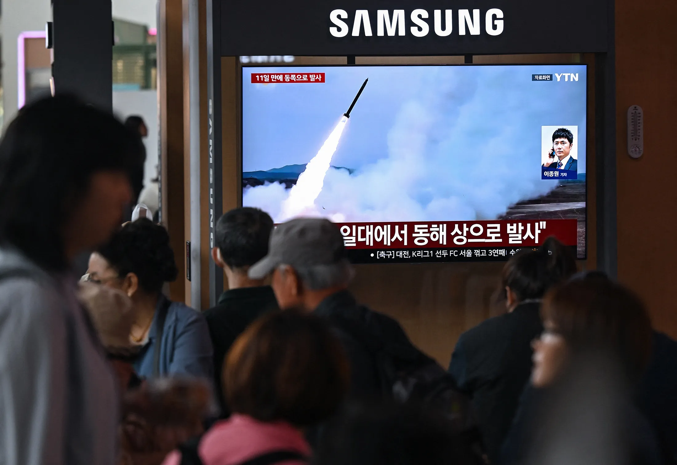 People watch a television screen showing a news broadcast with file footage of a North Korean missile test, at a train station in Seoul on April 19.