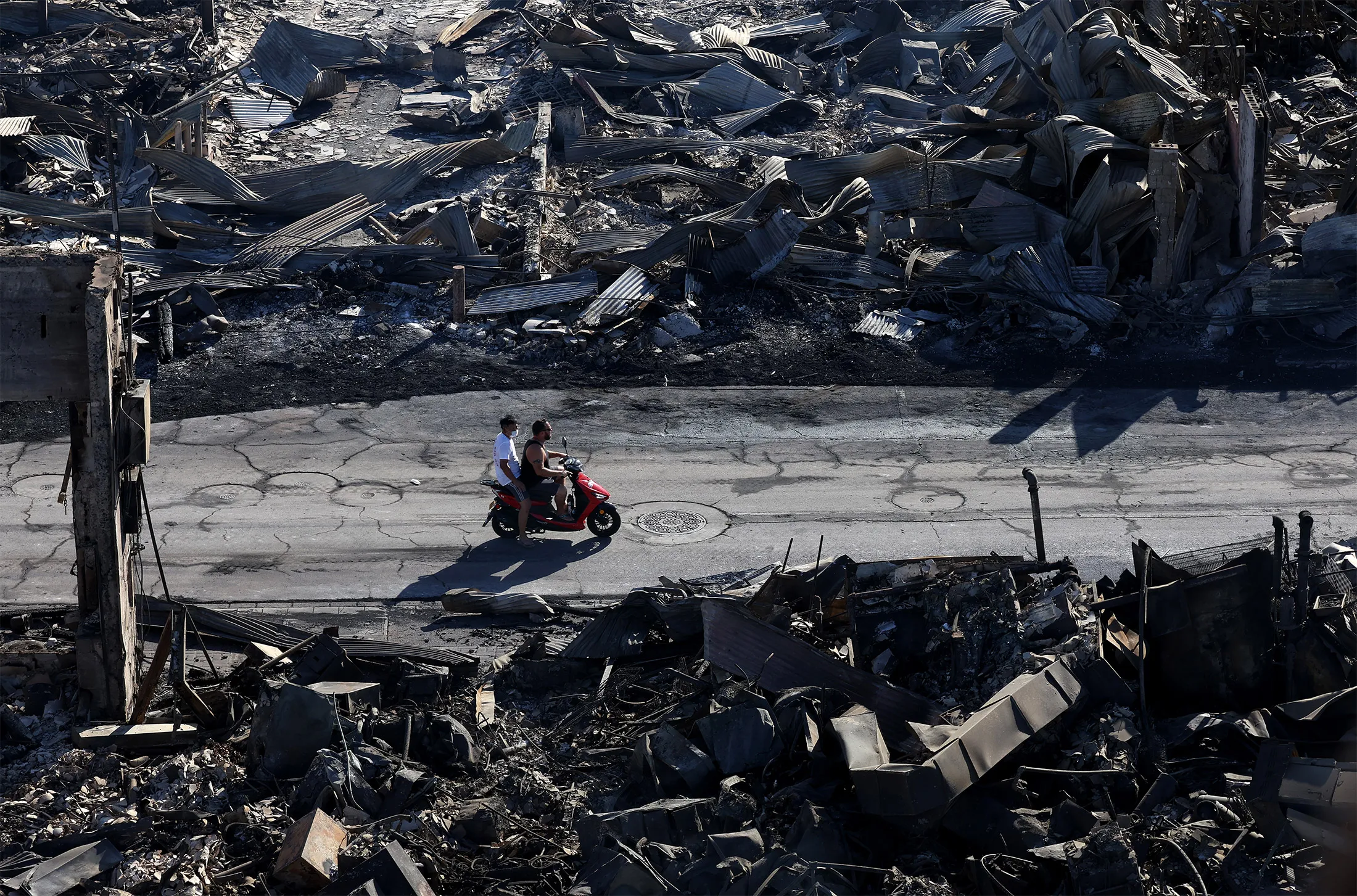 People ride a scooter past buildings destroyed by wildfires in Lahaina, Maui, Hawaii.